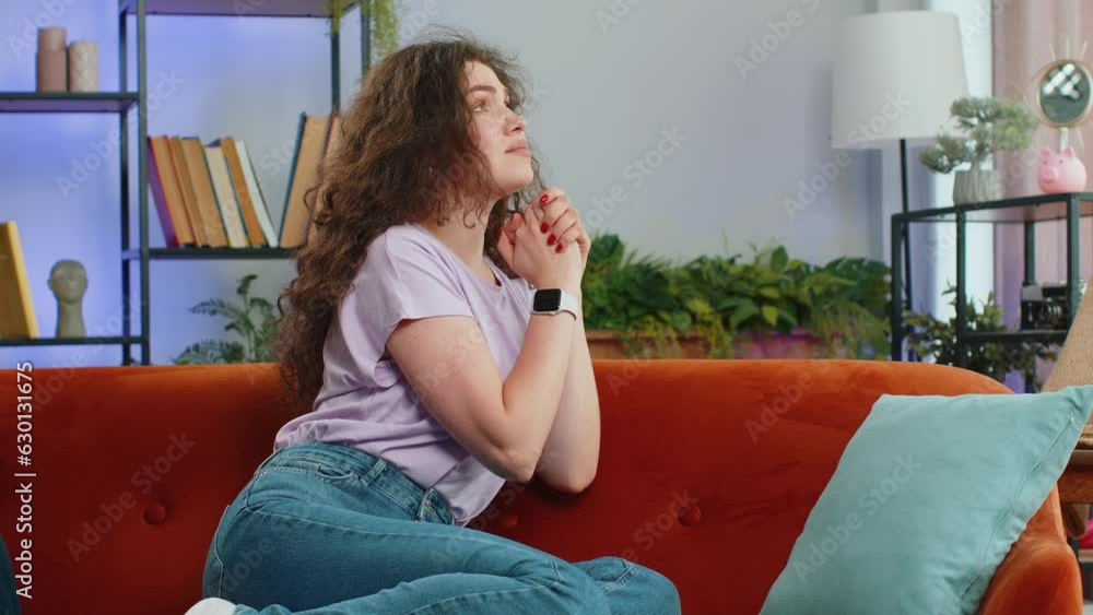 Please, God help. Young woman praying sincerely with folded arms, looking upward and making wish, asking with hopeful imploring expression, begging apology. Sad girl at home apartment room on sofa Please, God help. Young woman praying sincerely with folded arms, looking upward and making wish, asking with hopeful imploring expression, begging apology. Sad girl at home apartment room on sofa