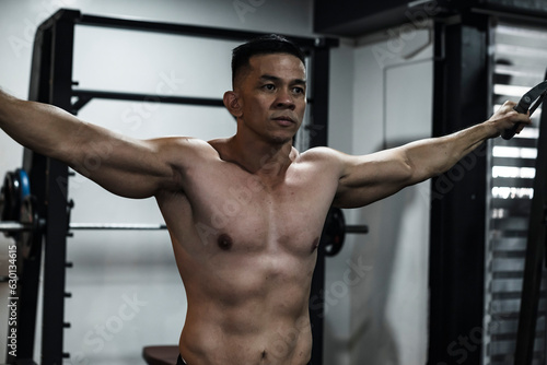 A sexy and handsome shirtless asian man does some cable crossovers. Chest day workout training at the gym.