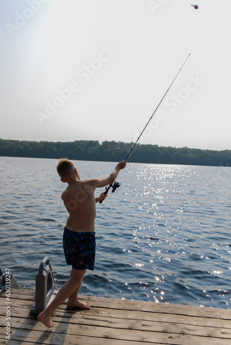 Childhood Delights: A Young Boy Enjoying Serene Fishing Moments from the Wooden Deck, Gently Casting His Fishing Rod into the Tranquil Waters of the Glittering Lake