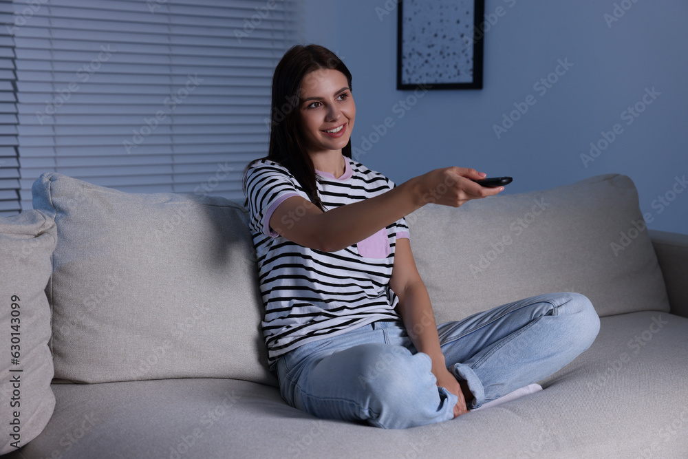 Obraz premium Happy woman changing TV channels with remote control at home
