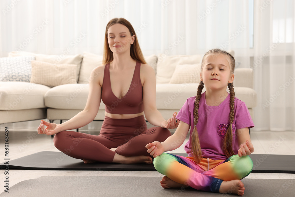 Mother with daughter in sportswear meditating together at home. Harmony and zen