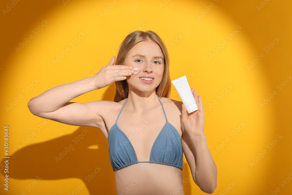 Beautiful young woman applying sun protection cream onto her face against orange background Beautiful young woman applying sun protection cream onto her face against orange background