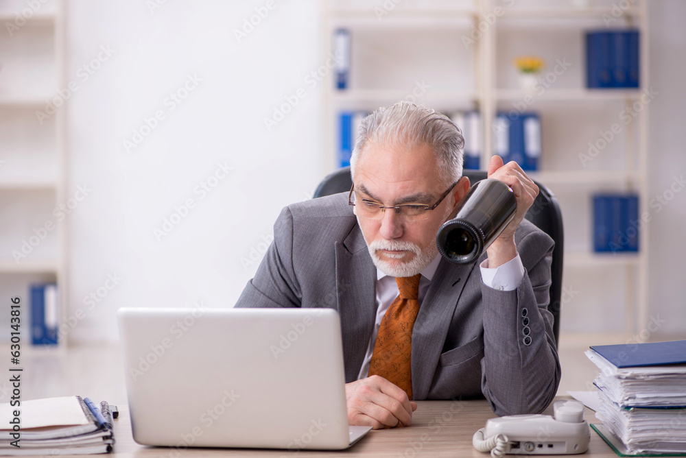 Old male employee drinking alcohol at workplace Old male employee drinking alcohol at workplace