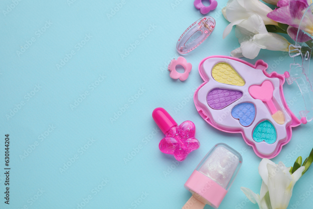 Decorative cosmetics for kids. Eye shadow palette, lipsticks, accessories and flowers on light blue background, flat lay. Space for text