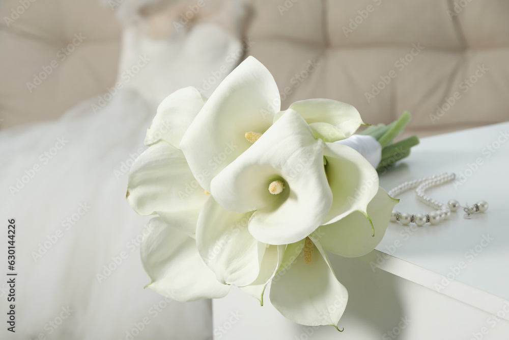 Beautiful calla lily flowers tied with ribbon and jewelry on white chest of drawers indoors Beautiful calla lily flowers tied with ribbon and jewelry on white chest of drawers indoors