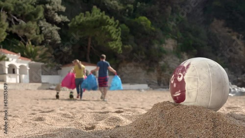 Friendly family with dogs leaves beach with waste bags after picnic in nature, they forgot Wilson volleyball on sand, responsible vacationers, clean up after yourself. Team of volunteers carry garbage photo