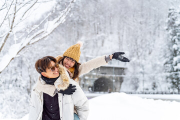 Happy Asian couple have fun playing snow ball during travel small town and forest mountain together in snowy day. Man and woman enjoy outdoor lifestyle travel in Japan in winter holiday vacation.