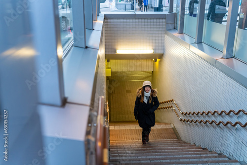 Young Asian woman walking up on staircase at subway station in the city at night. Attractive girl enjoy urban outdoor lifestyle travel city street by public transportation in Japan on winter vacation.