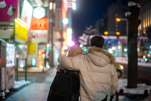 Asian couple dating and shopping at retail store street market together in the city at night. Man and woman enjoy and fun outdoor lifestyle nightlife walking city street in winter holiday vacation.