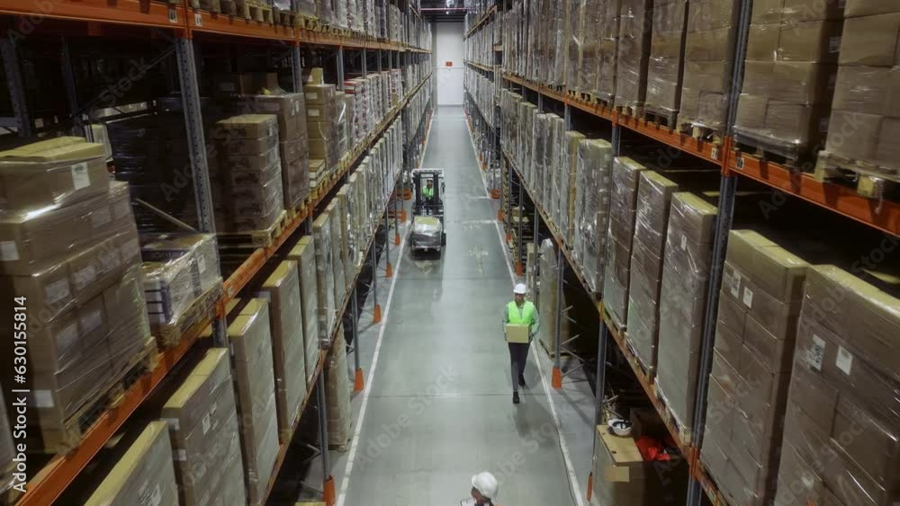 Worker Operating Hand Pallet Truck, Moving Cardboard Boxes Between Shelves Filled with Goods in Warehouse. People Work in Product Distribution Logistics Center Inside Worker Operating Hand Pallet Truck, Moving Cardboard Boxes Between Shelves Filled with Goods in Warehouse. People Work in Product Distribution Logistics Center Inside