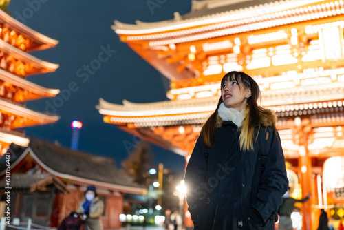 Young Asian woman travel at Sensoji Temple at Asakusa Tokyo, Japan at night. Attractive girl tourist travel Japan landmark famous place and walking city street market in winter holiday vacation.