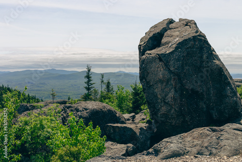vue sur le sommet d'une montagne avec un gros rocher en avant plan une forêt dans la vallée lors d'une journée d'été photo