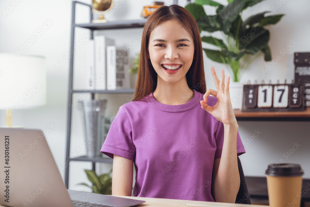 Young attractive female sitting at the desk and using laptop computer with shows ok sign. Young attractive female sitting at the desk and using laptop computer with shows ok sign.