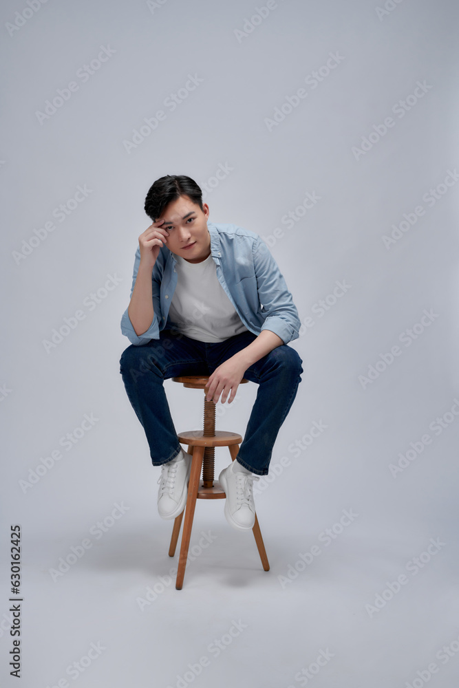 Young asian man seated on a chair isolated on white background.