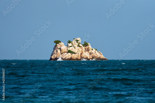 Beautiful rocky island over blue sky. A lonely beautiful high rocky island in the sea with waves.