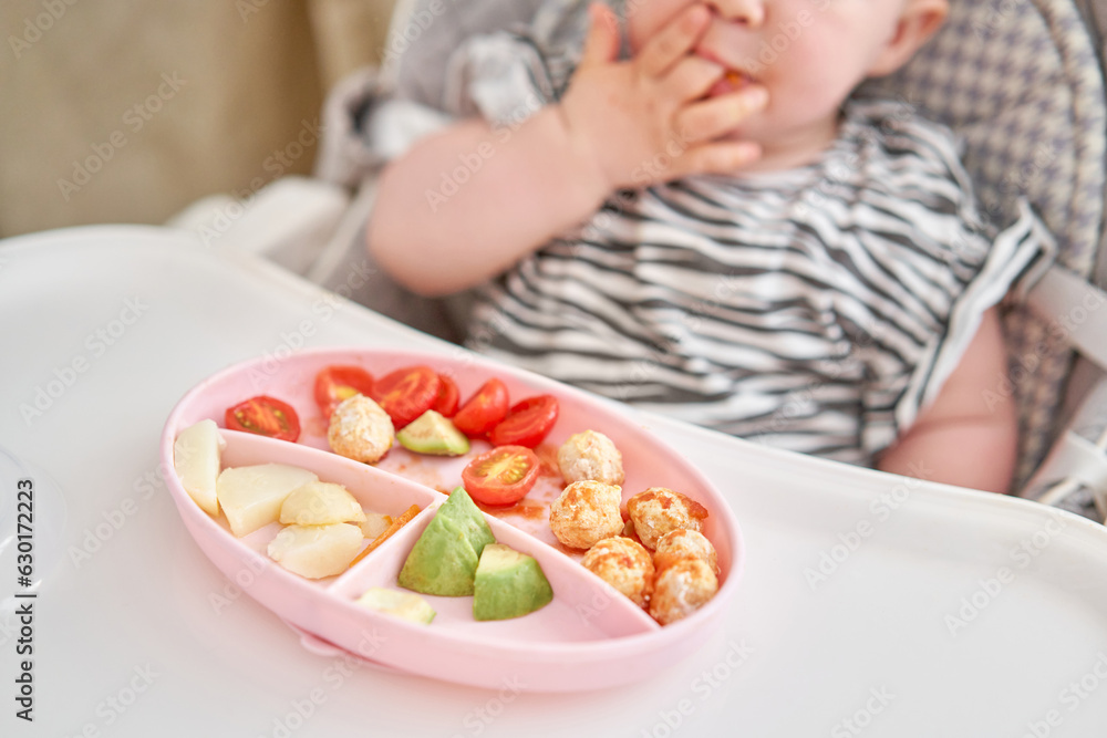 Cute child eats healthy food vegetables and meatballs from dietary meat steamed,. Portraits of a cute 10 months old baby girl. The baby sitting in a special high chair for babies.