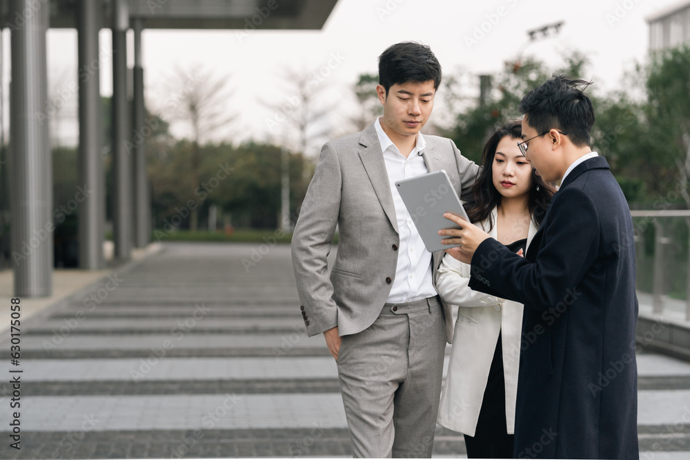 Asian business people using tablet computer and talking outdoors. Asian business people using tablet computer and talking outdoors.