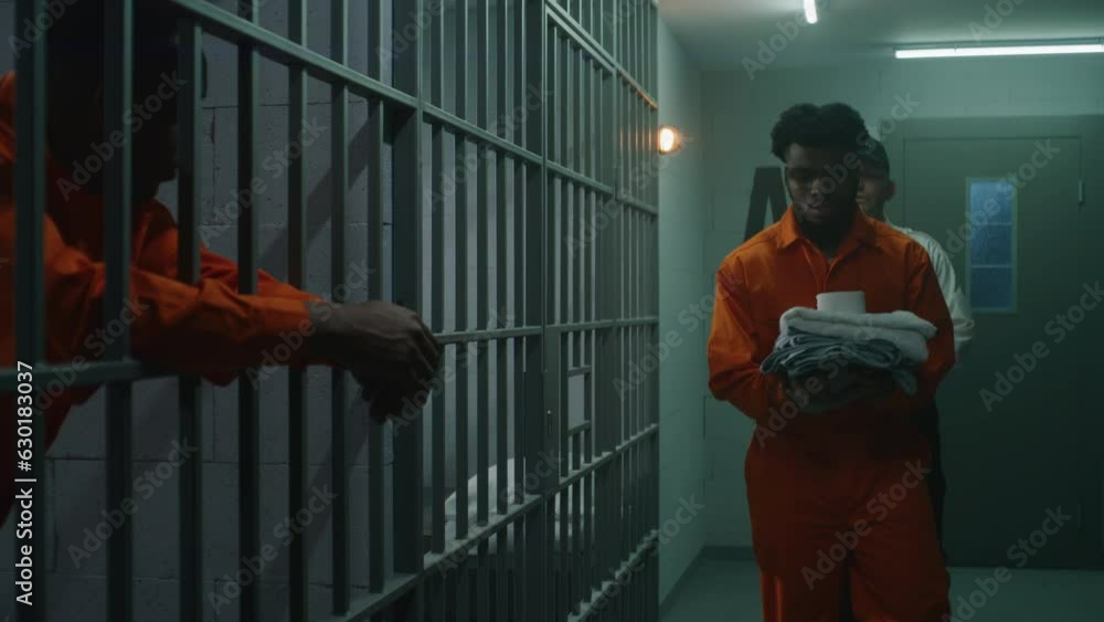 Warden brings new prisoner in jail cell and takes off his handcuffs. African American criminals serve imprisonment term in correctional facility or detention center. Guilty murderers in prison cells. Warden brings new prisoner in jail cell and takes off his handcuffs. African American criminals serve imprisonment term in correctional facility or detention center. Guilty murderers in prison cells.