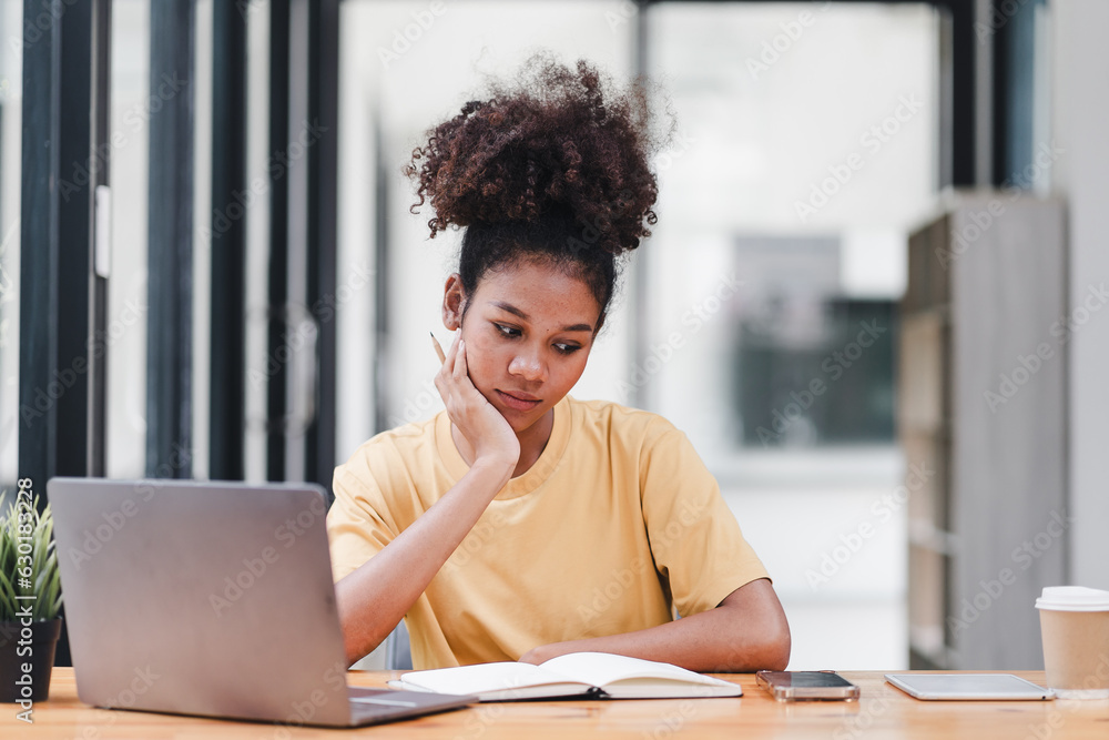 Young African American woman is taking notes in a notebook while watching a webinar video course. Afro american student listening to the lecture to study online through e-learning. Young African American woman is taking notes in a notebook while watching a webinar video course. Afro american student listening to the lecture to study online through e-learning.