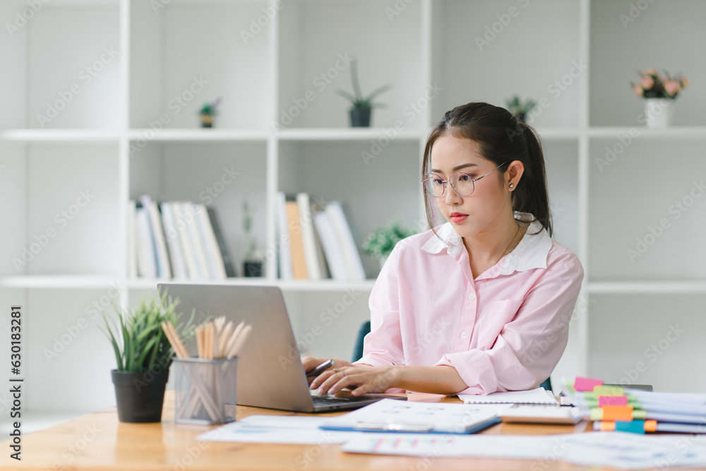 A portrait of a smiling, young, beautiful, professional, and confident millennial Asian businesswoman using a digital laptop to analyze sales data at a modern office. A portrait of a smiling, young, beautiful, professional, and confident millennial Asian businesswoman using a digital laptop to analyze sales data at a modern office.