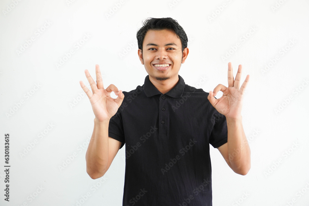 young Asian man smiling friendly while giving OK finger sign wearing black polo t shirt isolated on white background young Asian man smiling friendly while giving OK finger sign wearing black polo t shirt isolated on white background