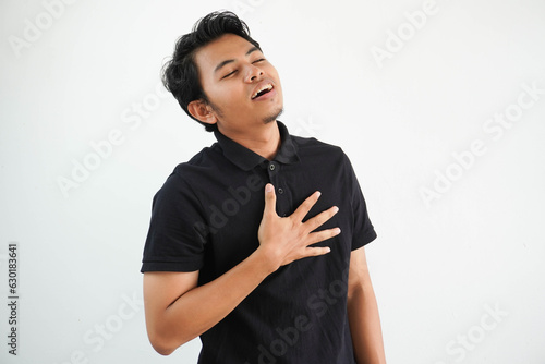 young asian man posing on a white backdrop laughing keeping hands on heart, concept of happiness. wearing black polo t shirt. photo