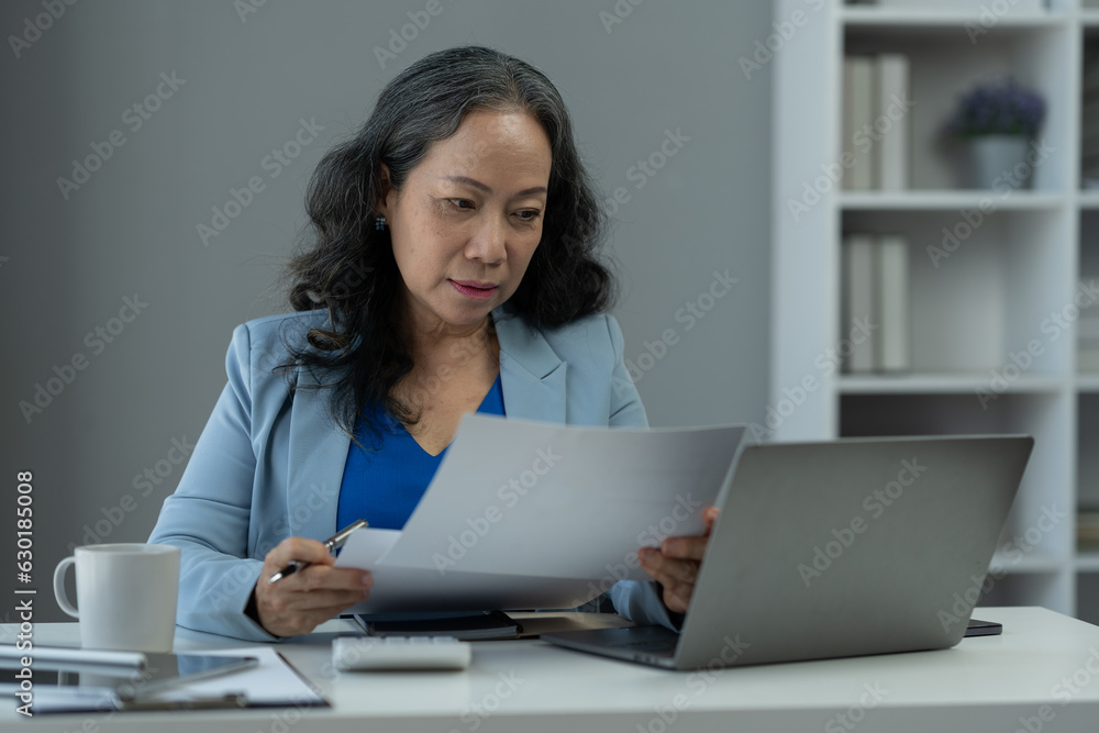 Retired businesswoman or senior executive looking at documents and recordings of online webinars on laptop computer. meeting to plan Analyze economic plans, taxes, office investments.