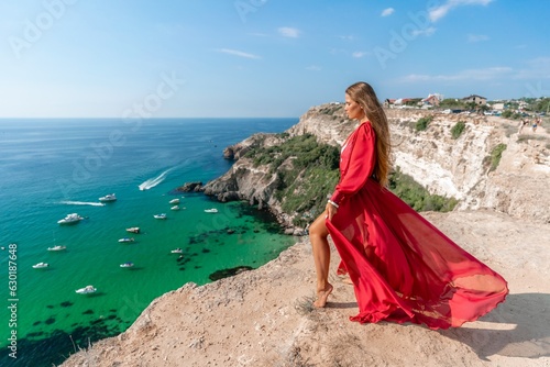 Red Dress Woman sea Cliff. A beautiful woman in a red dress and white swimsuit poses on a cliff overlooking the sea on a sunny day. Boats and yachts dot the background.
