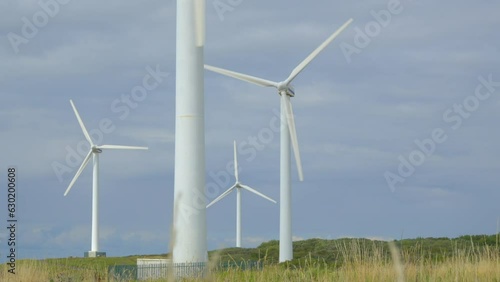 Wind turbines through blurred grasses with rise up reveal clearing grass and showing windmills against cloudy summer sky. Half speed slow motion. photo