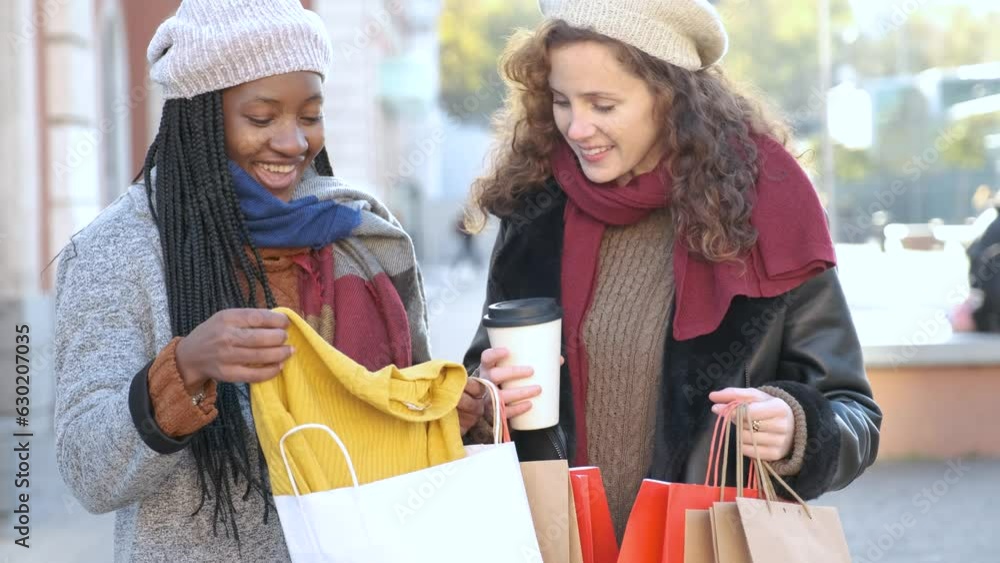 Two multiracial female friends looking the clothes they bought after shopping in winter. Two multiracial female friends looking the clothes they bought after shopping in winter.