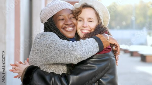 Two multiracial female happy friends hugging each other and smiling on city street. photo