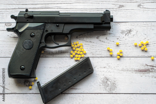 airsoft handgun with yellow bb, on white wooden background photo