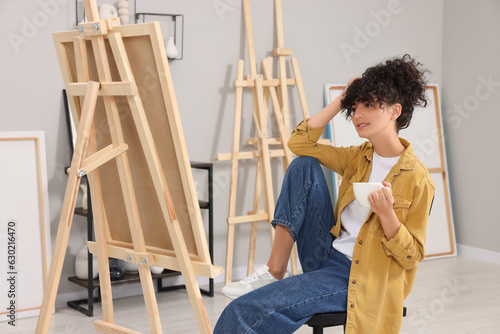 Young woman with cup near easel in studio
