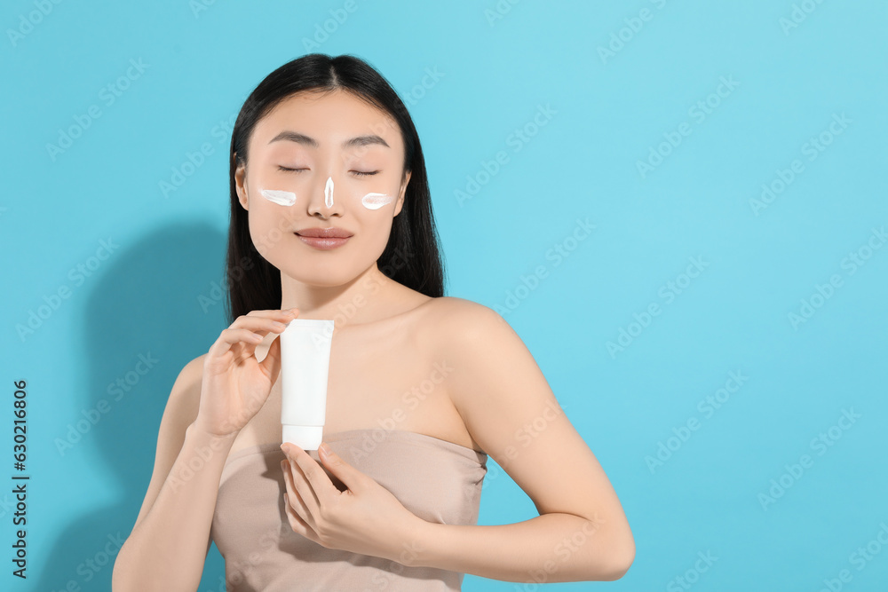 Beautiful young woman with sunscreen on her face holding sun protection cream against light blue background, space for text Beautiful young woman with sunscreen on her face holding sun protection cream against light blue background, space for text