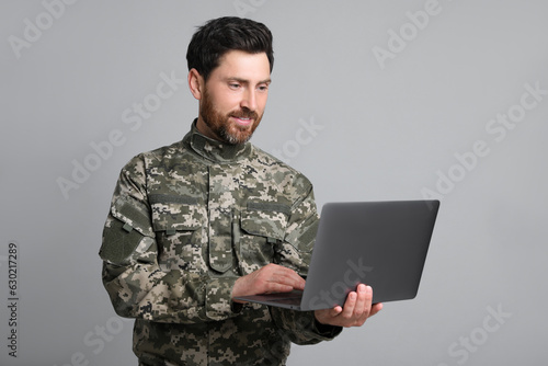 Soldier using laptop against light grey background. Military service photo