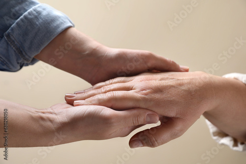 Woman holding hands with her mother on beige background, closeup