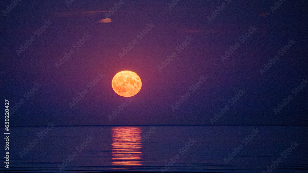 Naklejka premium Super moon full moon rising above Irish Sea with reflection