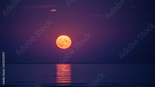 Super moon full moon rising above Irish Sea with reflection