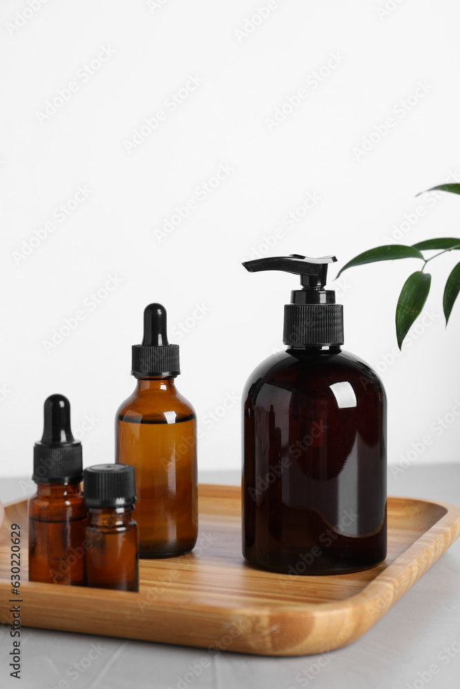 Different cosmetic products and leaves on grey table