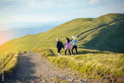 Three Young Girl Friends Walk Together Holding Hands into Beautiful Mountain Landscapes © andrii_popovych