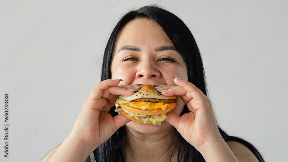 Dark-haired woman enjoys eating juicy burger from fast food restaurant. Plump lady eats junk food forgetting about own health and wellness