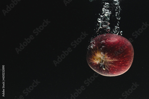Close up of red apple falling into water with copy space on black background