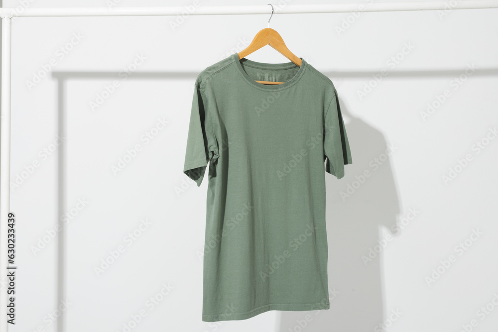 Fototapeta premium Green t shirt on hanger hanging from clothes rail with copy space on white background