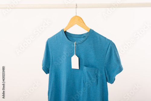 Blue t shirt with tag on hanger hanging from clothes rail with copy space on white background