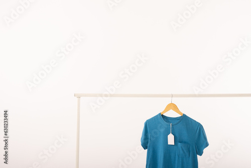 Blue t shirt with tag on hanger hanging from clothes rail with copy space on white background