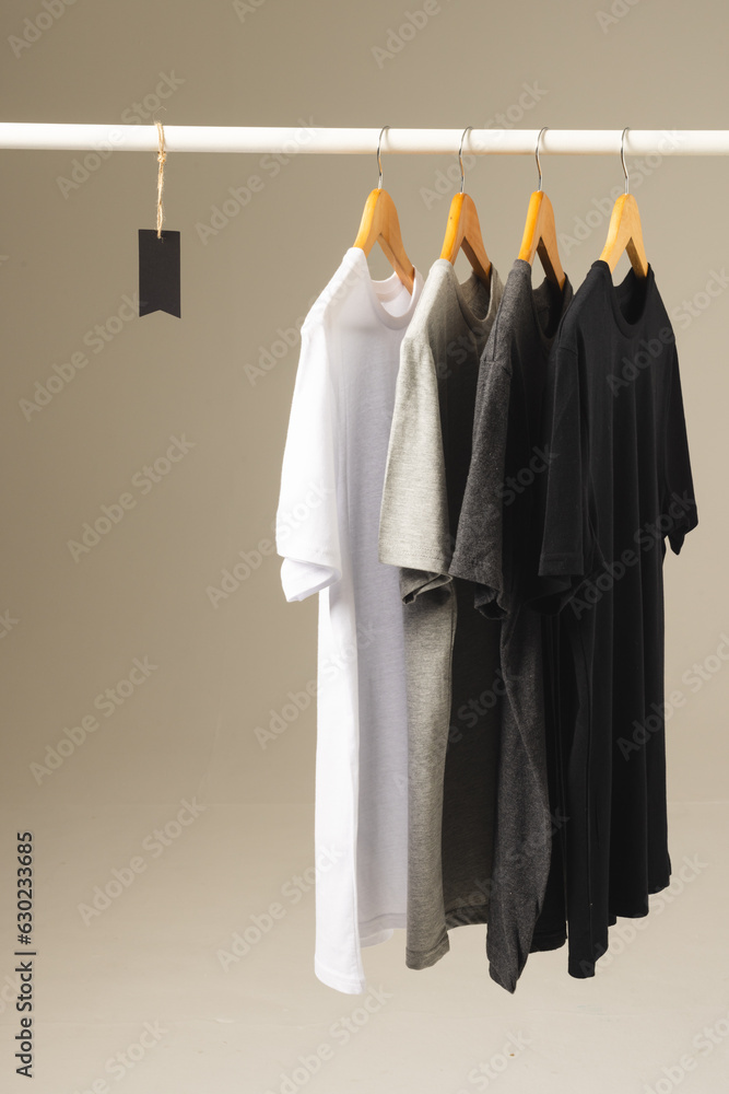 Fototapeta premium Four t shirts on hangers hanging from clothes rail and copy space on grey background