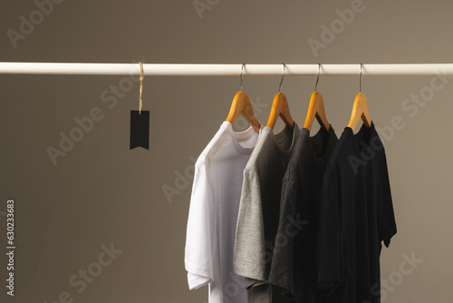 Four t shirts on hangers hanging from clothes rail and copy space on grey background