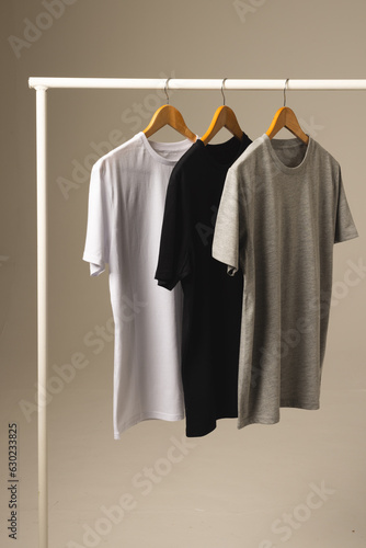 Three t shirts on hangers hanging from clothes rail and copy space on grey background