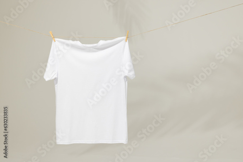 White t shirt hanging from clothes line with pegs and copy space on grey background