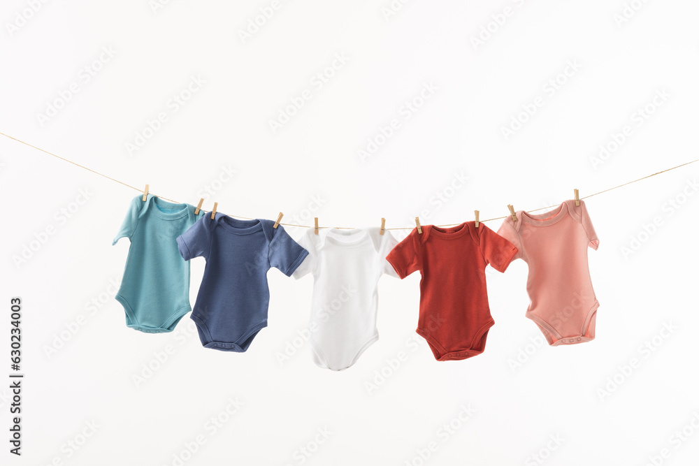 Multi coloured baby grows hanging from clothes line with pegs and copy space on white background Multi coloured baby grows hanging from clothes line with pegs and copy space on white background